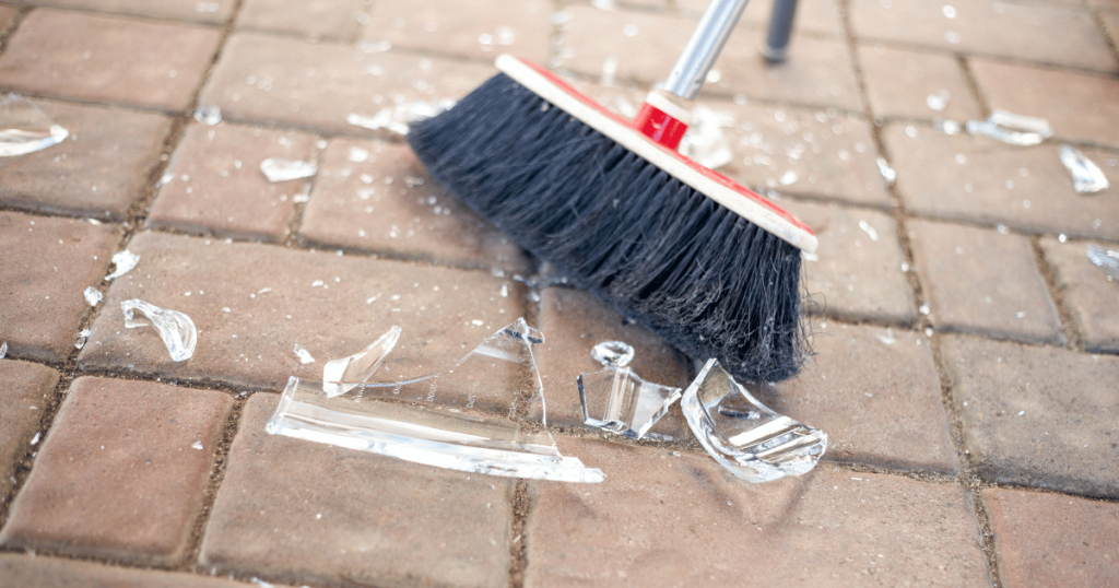 A broom sweeping broken glass shards off a brick floor as shown in Maggy Maid's guide on how to clean broken glass in quick and simple steps.