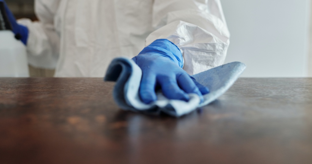 A cleaner in a protective suit and blue gloves wiping a surface with a microfiber cloth as shown in Maggy Maid's guide on how to clean broken glass in quick and simple steps.