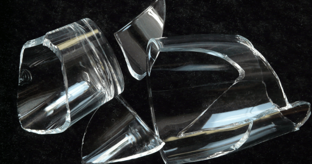 Large clear glass shards scattered on a dark floor as shown in Maggy Maid's guide on how to clean broken glass in quick and simple steps.