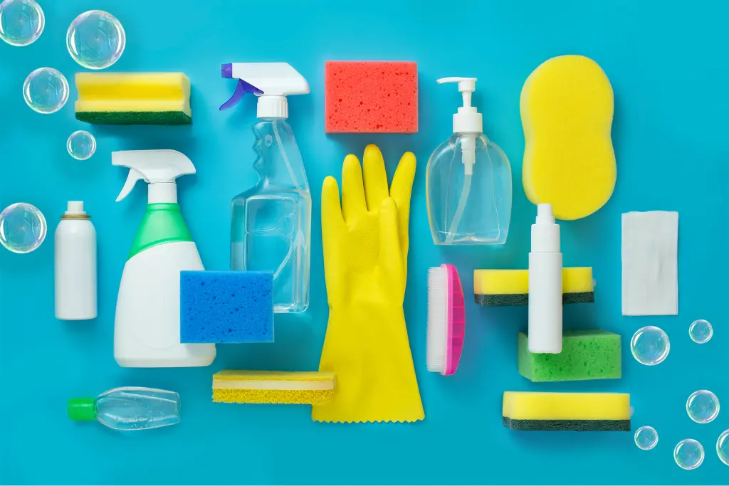Alt text: Maggy Maid professional cleaning supplies flat lay including spray bottles, yellow rubber gloves, colorful sponges, and soap dispenser on a teal background