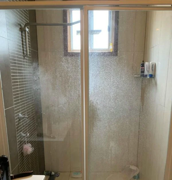 Maggy Maid bathroom deep cleaning showing heavy soap scum and hard water stains on glass shower doors and tiled shower enclosure