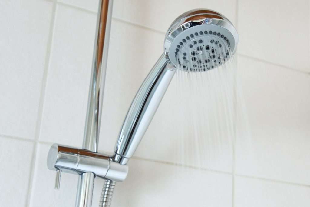 Maggy Maid professionally cleaned bathroom with a sparkling chrome handheld shower head spraying water against white tiles