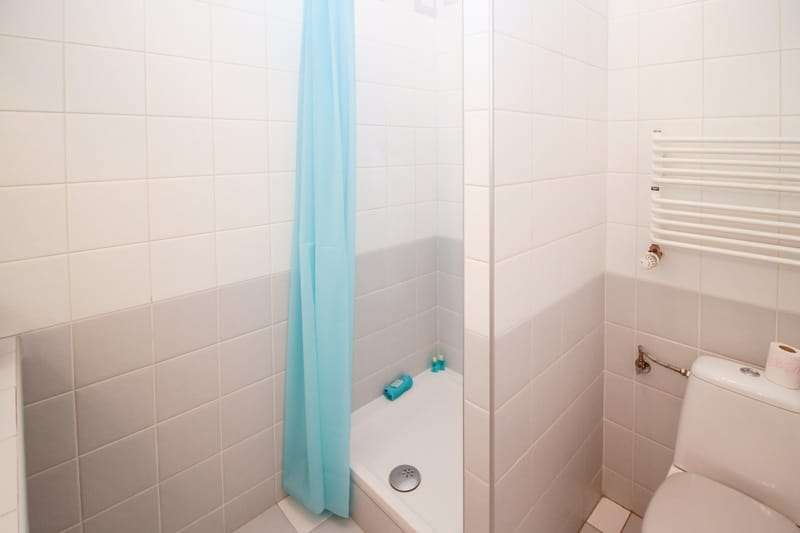 Maggy Maid professionally cleaned bathroom with white tiles, bathtub, light blue shower curtain, toilet, and heated towel rack